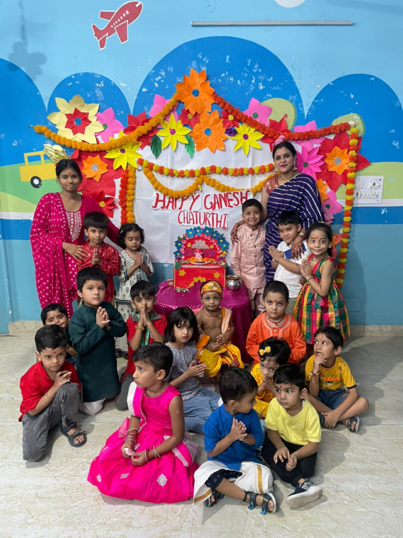 Children celebrating Ganesh Chaturthi at Udayan Kidz with colorful decorations, a clay idol of Lord Ganesha, and festive activities like dancing and singing.