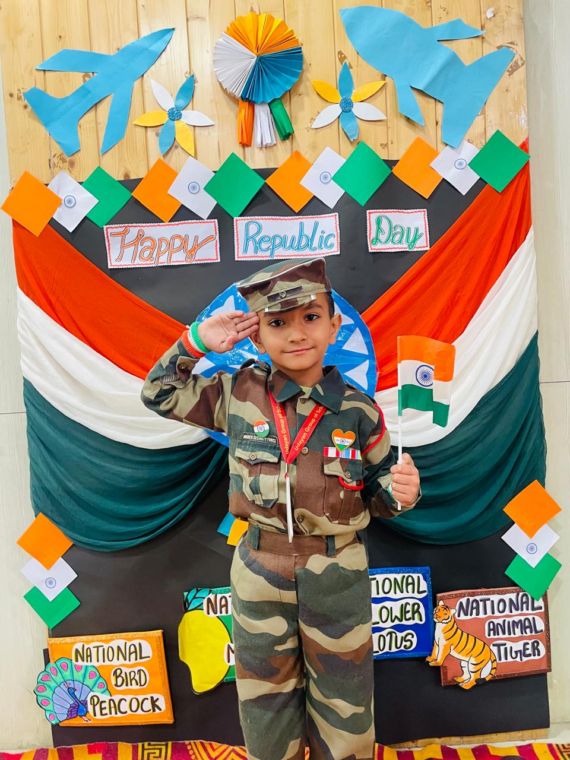 A young Udayan Kidz preschool student dressed as a soldier, saluting with a patriotic backdrop featuring the Indian flag and national symbols.