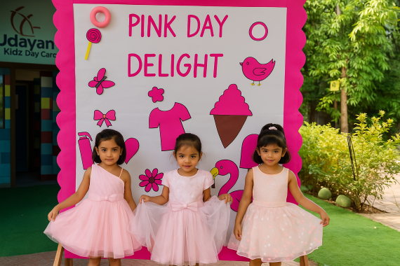 Three preschool girls dressed in pink outfits standing in front of a Pink Day Delight display board at Udayan Kidz, celebrating colour learning through fun classroom activities.